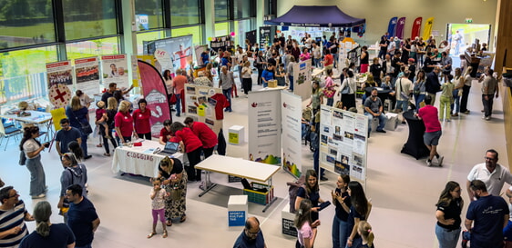 Informationsveranstaltung in heller Halle. Viele Menschen an St&auml;nden, Poster und Roll-Ups zu verschiedenen Themen.